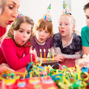 51585948 - child on birthday party blowing candles on cake being helped by friends and the mother